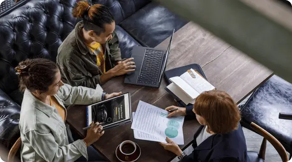 三個人坐在桌旁的俯視圖,其中一人正在查看文件,一人正在使用 Lenovo 平板電腦,還有一人正在使用 Lenovo 筆記型電腦。