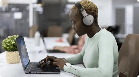 一位女士戴著耳機坐在桌前使用 Lenovo 筆記型電腦的側面視圖。